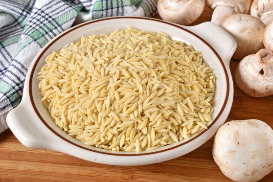 Bowl of raw orzo pasta and mushrooms on a cutting board with a kitchen towel